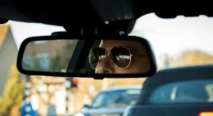 Chauffeur achter het stuur met zonnebril, gezien in achteruitkijkspiegel
